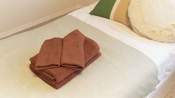 A neatly made bed with a folded brown towel and a pillow with a striped pillowcase.