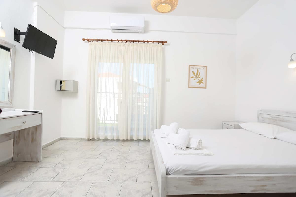 Une chambre d’hôtel comprenant un lit, une table de chevet, un bureau avec une chaise, un téléviseur à écran plat fixé au mur et une fenêtre avec des rideaux.