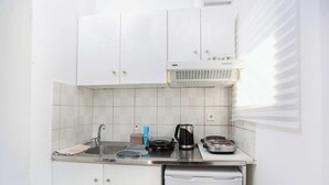 Een kleine keuken met witte kasten, een roestvrijstalen spoelbak, een koffiezetapparaat en een vaatwasser.