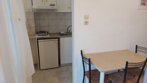 Een compacte keuken met een kleine koelkast, een fornuis en een spoelbak. Er is een tafel met twee stoelen.