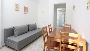Een kamer met een grijze bank, een houten eettafel en stoelen. Er hangen fotolijstjes aan de muur.