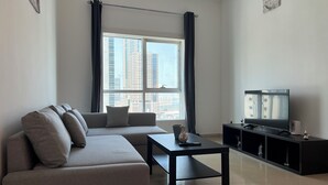 A modern living room with a grey sofa, a coffee table, a TV on a black stand, and a large window with curtains.