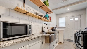 A kitchen with white cabinets, a granite countertop, a stainless steel sink, a microwave, a stove, and a window. - 2BR Cozy House Near Paseo the Art District (Oklahoma City)