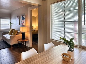 A modern hotel room with a wooden dining table, a sofa, a small side table, and a potted plant. - Cozy Charm Studio W 2BR I Fully Furnished (Midwest City)