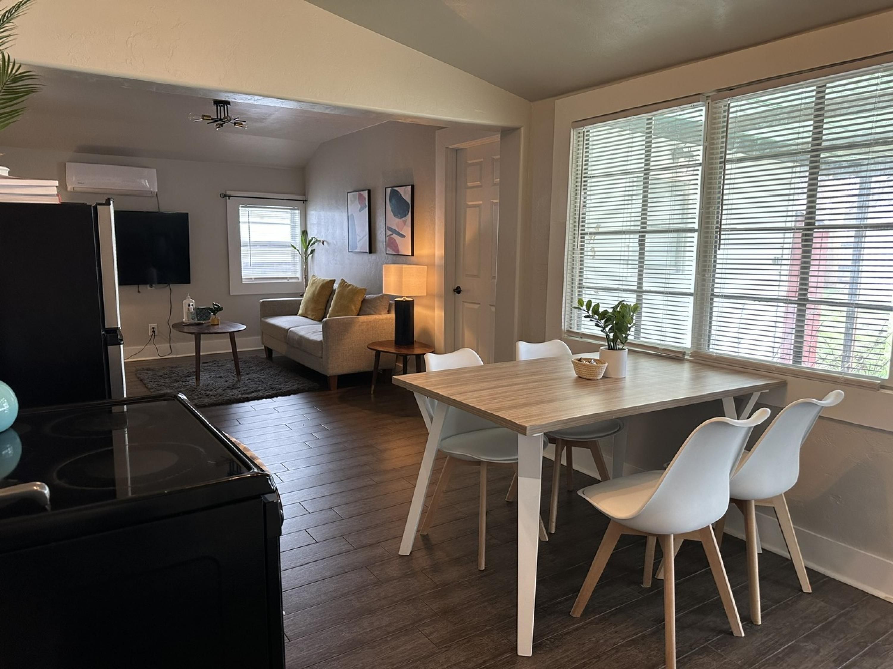 A modern living room with a sofa, a dining table with chairs, a TV, and a kitchen area with a refrigerator.