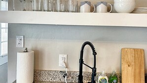 Una cucina con piano di lavoro in granito, rubinetto nero, porta asciugamani, flacone di detersivo per piatti e tagliere.
