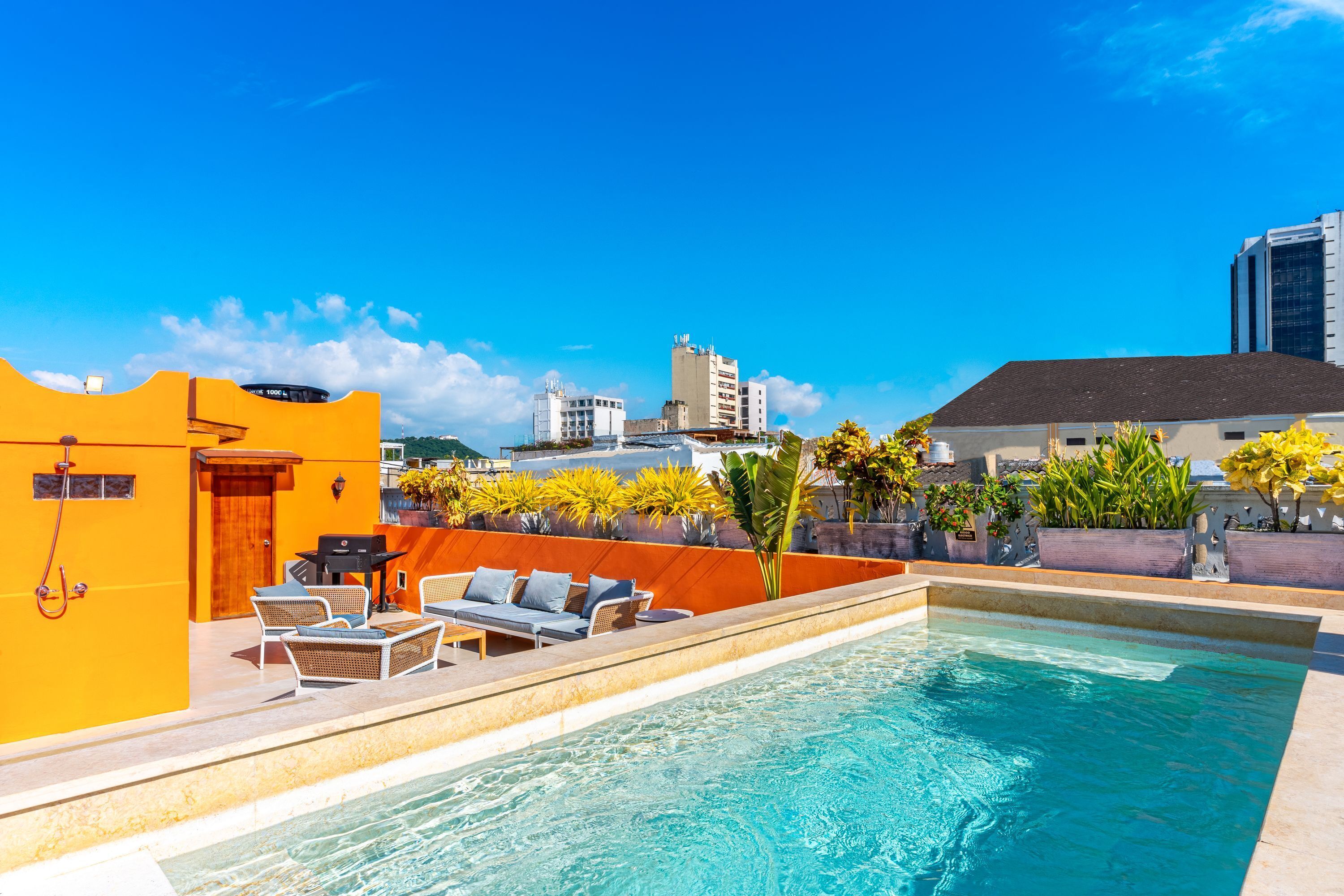 Piscina no terraço com espreguiçadeiras e uma pequena mesa, rodeada por paredes alaranjadas e plantas em vasos.