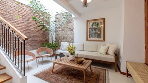 A living room with a wooden coffee table, two wicker chairs, a sofa, and a staircase with a metal railing. - Casa Cuero - Rooftop Pool - Historic Center (Cartagena)