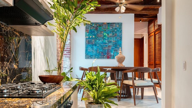 A modern kitchen with a marble countertop, a gas stove, and a dining area with a wooden table and chairs. - Casa Cuero - Rooftop Pool - Historic Center (Cartagena)