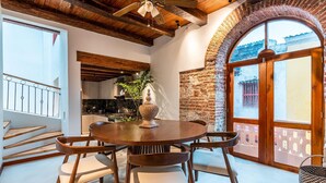 A dining area with a round wooden table and chairs, a ceiling fan, and a view of the outside through a large arched window. - Casa Cuero - Rooftop Pool - Historic Center (Cartagena)