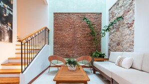 A modern living room with a wooden table, two cushioned chairs, a sofa, and a staircase with a metal railing. - Casa Cuero - Rooftop Pool - Historic Center (Cartagena)