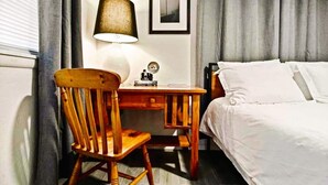 Une chambre d’hôtel avec un lit, une chaise en bois, un bureau avec une lampe et un tableau encadré au mur.