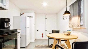 Une cuisine compacte équipée d’une cuisinière, d’un four à micro-ondes et d’un réfrigérateur. On y trouve une table à manger avec des chaises et un luminaire suspendu.