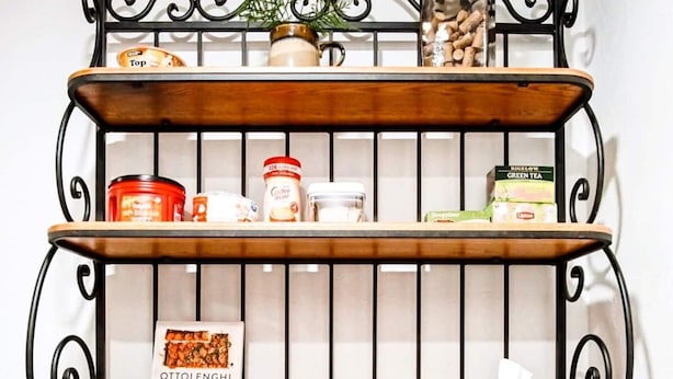 Une cuisine avec un plan de travail en bois, une étagère en métal où sont rangés des bocaux et une plante, et un meuble sous l’étagère.