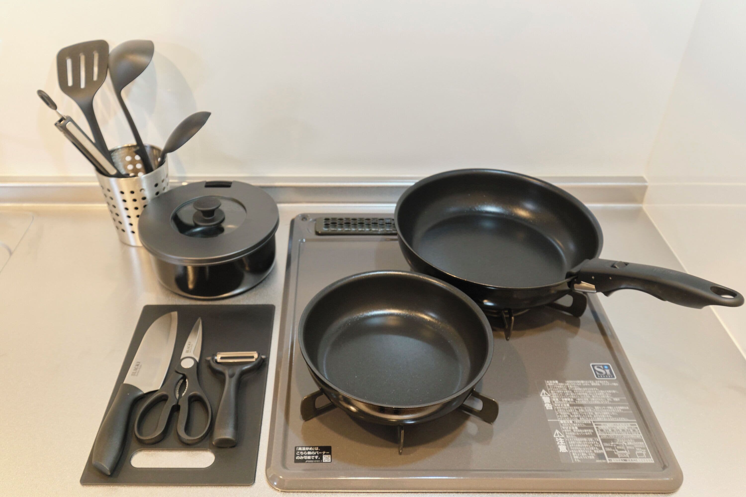 A kitchen counter with a frying pan, a pot, a spatula set, and a pair of scissors.