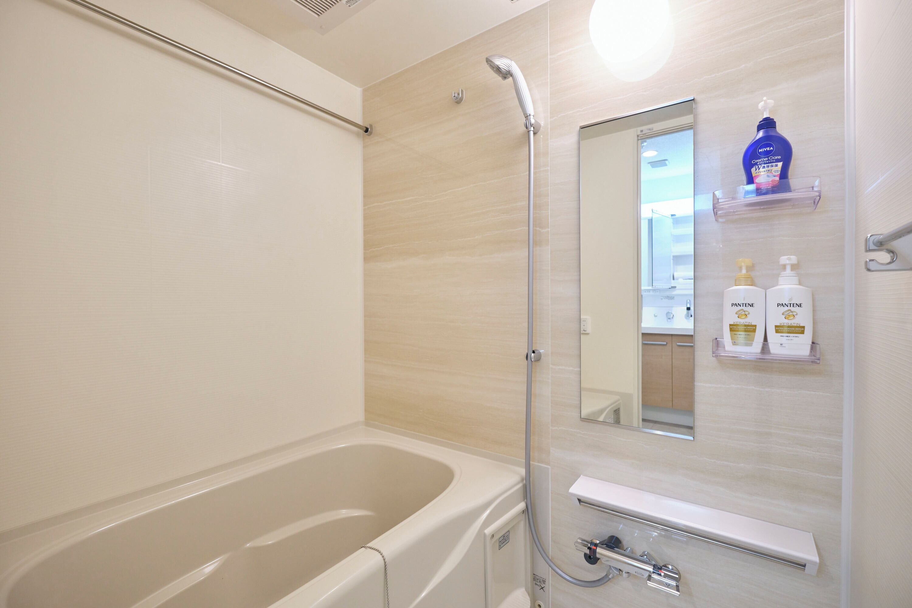 A bathroom with a bathtub, a shower, and a mirror. There are two bottles of Pantene shampoo and conditioner on a shelf.