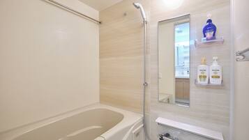 A bathroom with a bathtub, a shower, and a mirror. There are two bottles of Pantene shampoo and conditioner on a shelf.