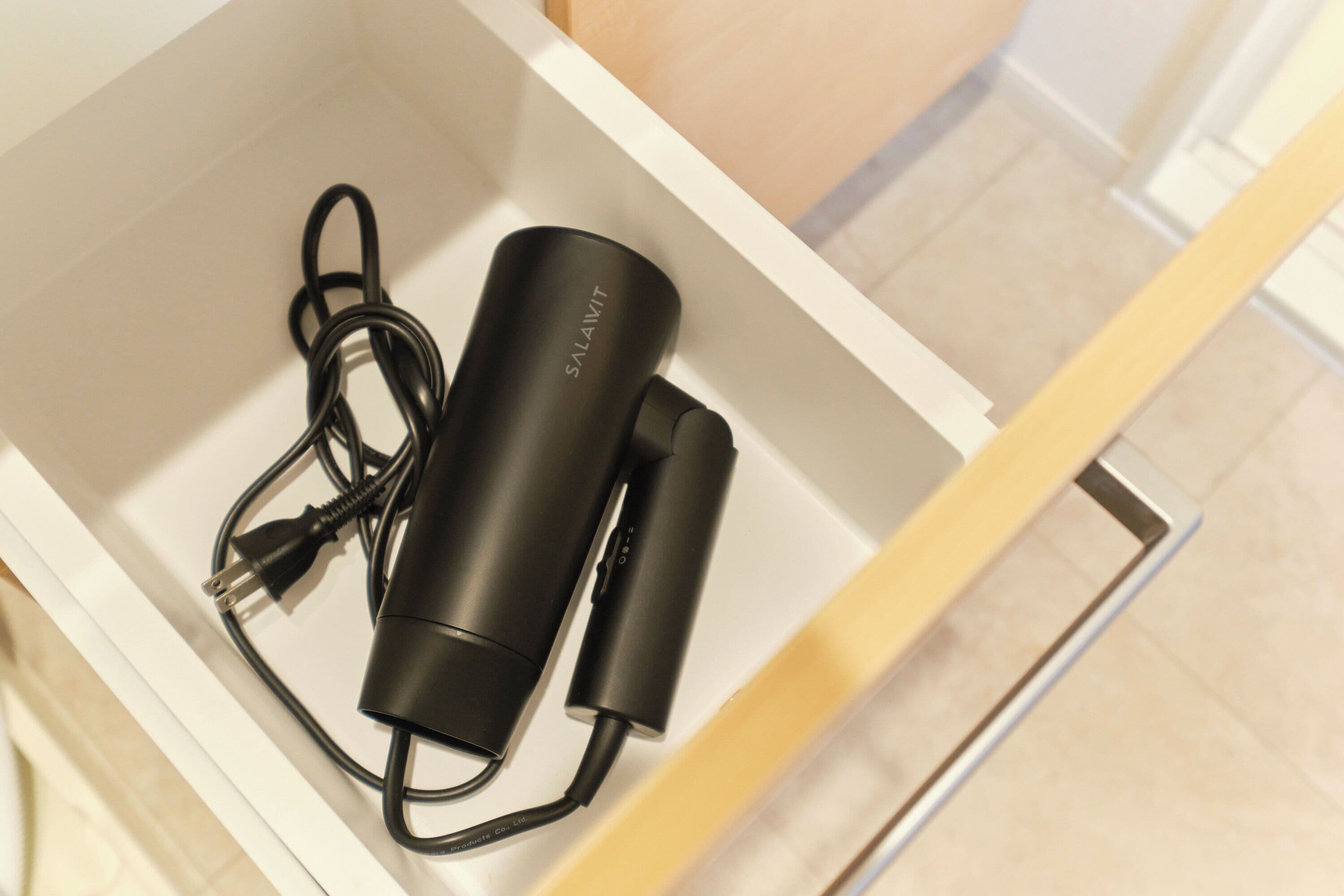 Un cajón blanco con un power bank negro y su cable en su interior.