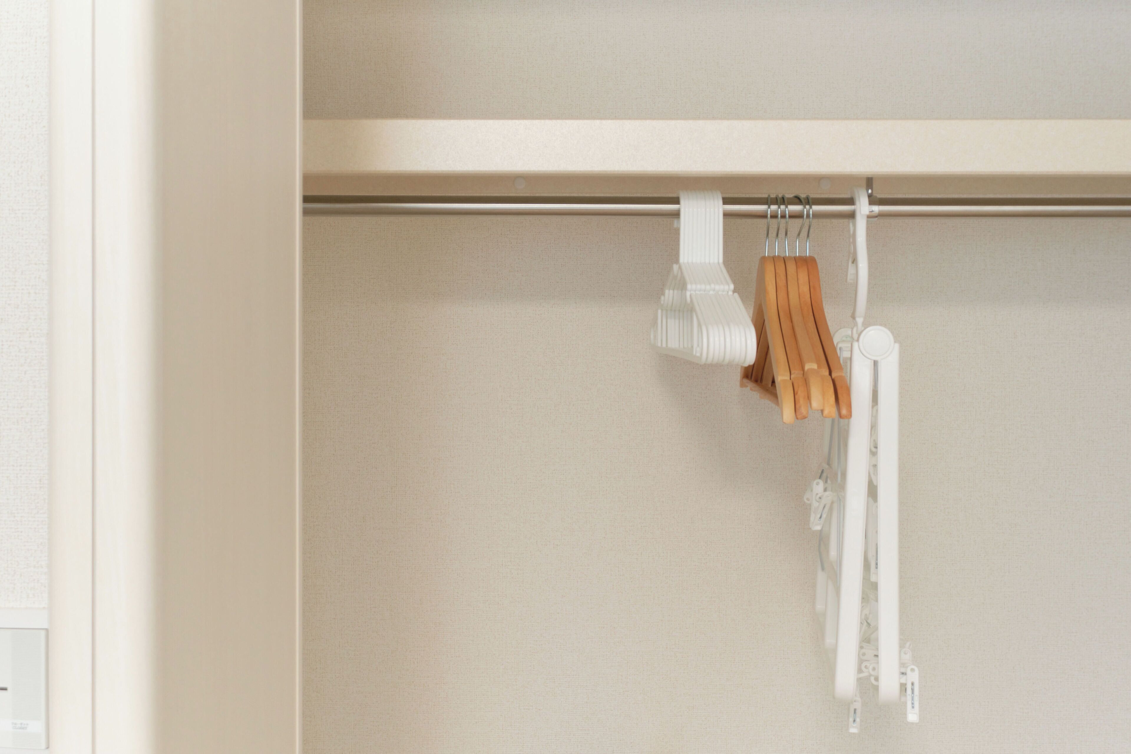 A closet with wooden hangers and white hangers on a rod.