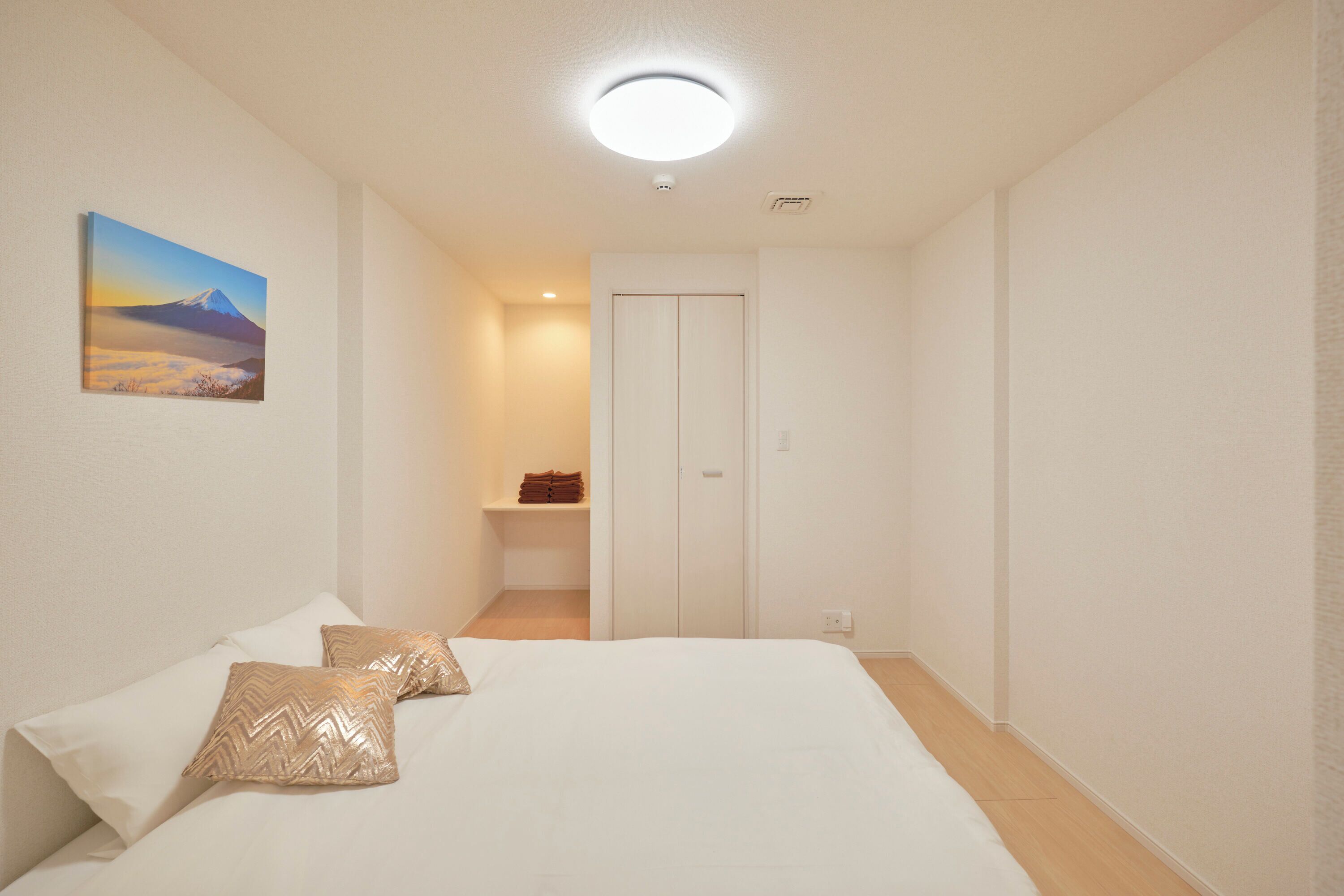 A bedroom with a bed, pillows, a painting, a closet, and a shelf with towels.