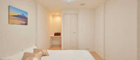 A bedroom with a bed, pillows, a painting, a closet, and a shelf with towels.