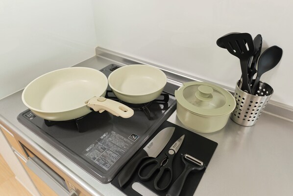 Una cocina con dos sartenes verde claro, una espátula negra, una olla y un recipiente para utensilios.