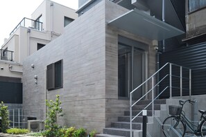Un edificio moderno con fachada gris, una escalera que lleva a un balcón, y una bicicleta estacionada afuera.