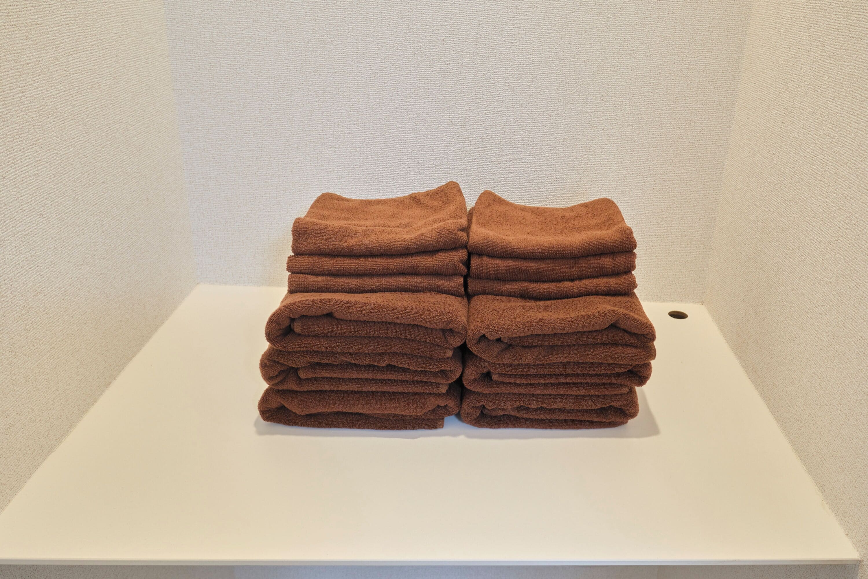 A stack of brown towels on a white rectangular surface against a plain wall.