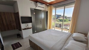 A bedroom with a large bed, a wardrobe, a television, and a sliding glass door to the outside. - Panchavati Resto and Spa (Mahabaleshwar)
