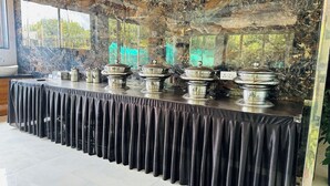 A buffet table with covered dishes, a bowl, and a pitcher, set against a stone wall with a view of greenery. - Panchavati Resto and Spa (Mahabaleshwar)