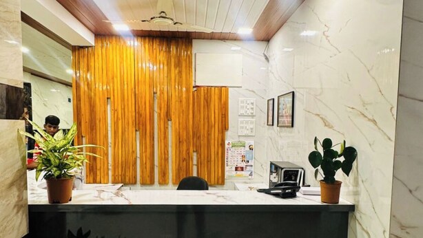 A reception area with a marble counter, wooden panel backdrop, ceiling fan, and potted plants. - Panchavati Resto and Spa (Mahabaleshwar)