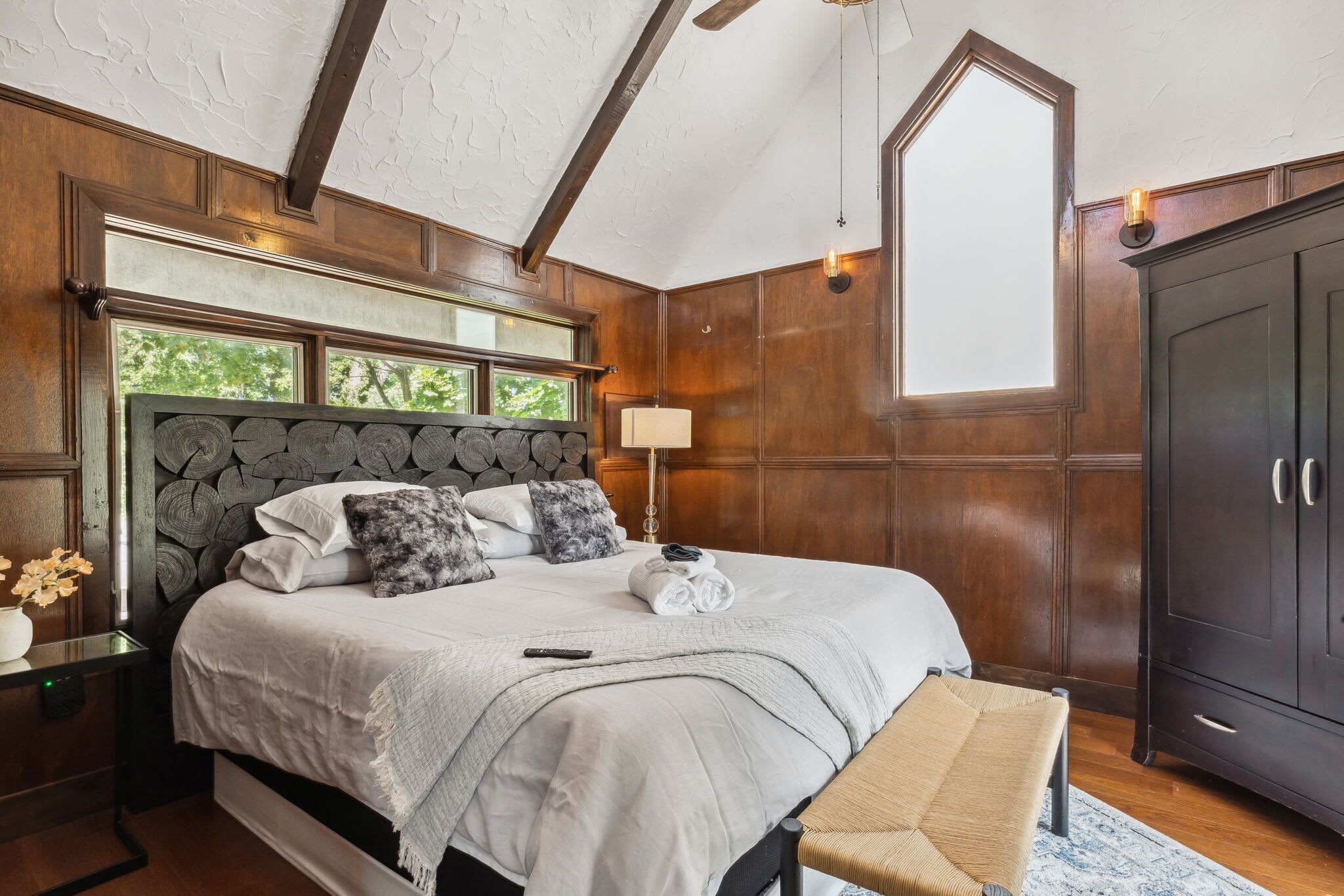 Ein Schlafzimmer mit einem großen Bett, Holzwandverkleidung, einem Nachttisch, einer Lampe und einem Kleiderschrank.
