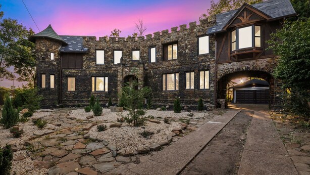 Una casa de estilo castillo de piedra con un camino de entrada que lleva a un garaje.