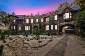 Una casa de estilo castillo de piedra con un camino de entrada que lleva a un garaje.