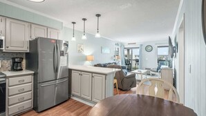 A modern kitchen with a stainless steel refrigerator, a coffee maker, and a dining area with a wooden table and chairs. - Ocean Forest Villas Unit D304 - Ocean view (Myrtle Beach)