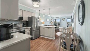 A modern kitchen with stainless steel appliances, a dining area with wooden chairs, and a view of the outdoors. - Ocean Forest Villas Unit D304 - Ocean view (Myrtle Beach)