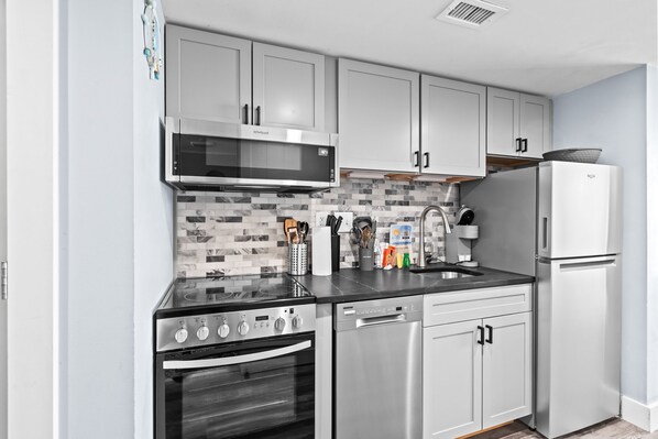 A modern kitchen with white cabinets, a stainless steel range, a dishwasher, and a refrigerator.