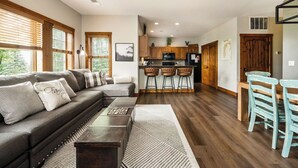 A modern living space with a sofa, coffee table, and bar stools. - Mountain Creekside: Hot Tub: Golf (Boyne City)