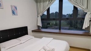 A neatly made bed with white linens and a rolled towel, a window with curtains, and a view of trees outside. - Cityview 2BR Country Garden Danga Bay @ Natol (Johor Bahru)