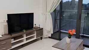 A modern living room with a flat-screen TV, a coffee table, and a balcony with a view. - Cityview 2BR Country Garden Danga Bay @ Natol (Johor Bahru)