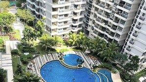 A large, curved swimming pool surrounded by palm trees and a landscaped area, with high-rise buildings in the background. - Cityview 2BR Country Garden Danga Bay @ Natol (Johor Bahru)