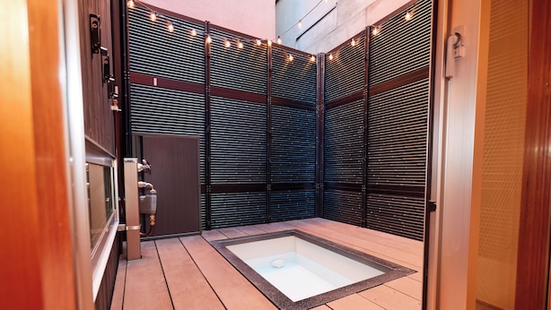 A modern spa area with a wooden deck, a glass-enclosed hot tub, and a series of black louvered walls. - Asakusa Ryokan Vacation Rental Tokyokoso (Tokyo)