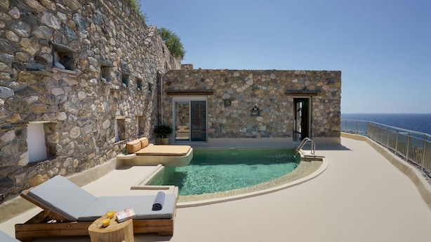 A stone-walled infinity pool with lounge chairs, a small table, and a door leading to a covered area. - Stylish Villa w/Private Pool & BBQ near Elafonissi (Chania)