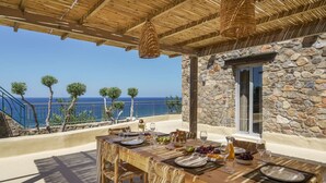 A wooden table set for dining with a stone wall and a view of the sea. - Stylish Villa w/Private Pool & BBQ near Elafonissi (Chania)
