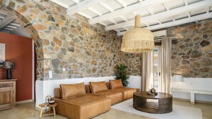 A living room with a stone wall, a brown sofa, a round wooden coffee table, and a hanging light fixture. - Stylish Villa w/Private Pool & BBQ near Elafonissi (Chania)