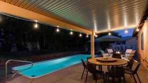 Ein Außenpoolbereich mit überdachter Terrasse, einem runden Tisch und Stühlen.
