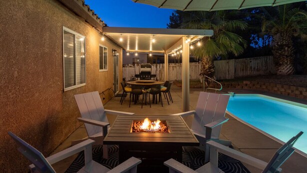 Ein Außenbereich mit Terrasse, Pool, Feuerstelle und überdachter Sitzgruppe mit Stühlen und Tisch.
