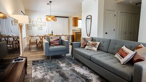 Ein modernes Wohnzimmer mit einem grauen Sofa, einem blauen Sessel und einem Essbereich mit einem Holztisch und Stühlen.