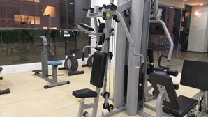 Un gimnasio con diferentes máquinas de ejercicio, un amplio ventanal y vista a un edificio.