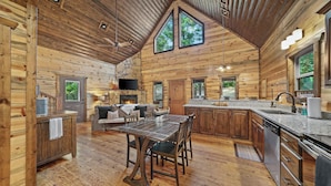 A log cabin interior with a dining area, kitchen, and a fireplace.
